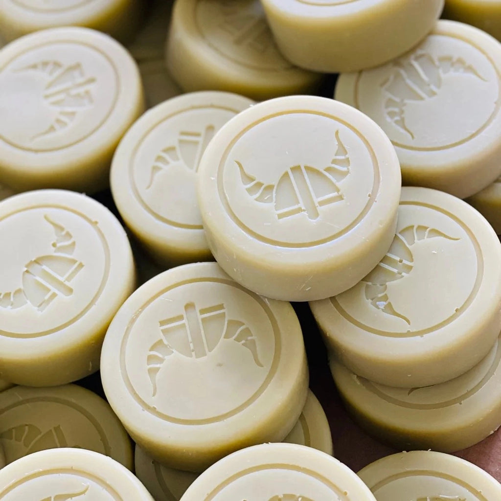Close-up of round artisan Valor Woodsman Scent - Cedarwood & Lemon Iron Bark shaving soap pucks with embossed Viking-style helmet design from Valor Organics.