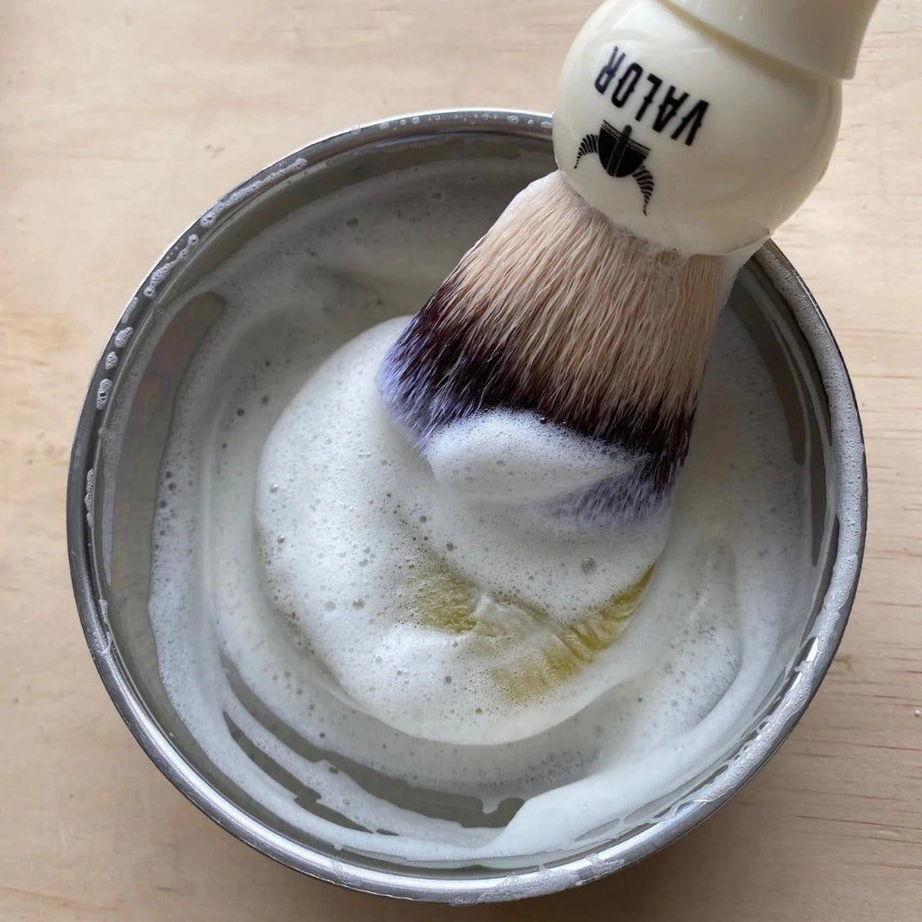 Shaving brush with a bowl of lather on a wooden surface